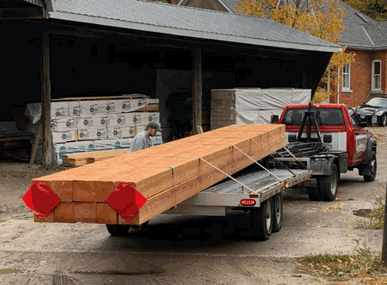 Fir timbers stacked onto a fladbed trailer behind a red pickup truck